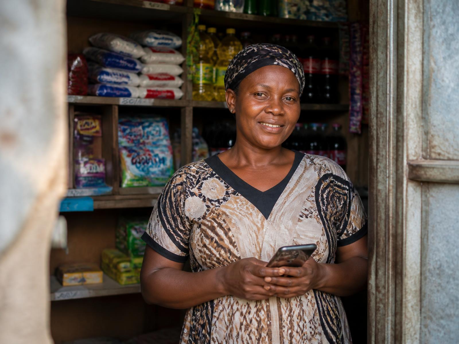Shop owner in Dar es Salaam standing in her duka with her phone